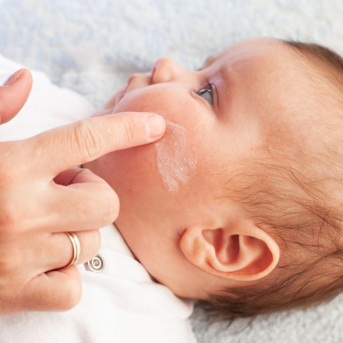 Baby lying on a white blanket with a hand gently touching its face.