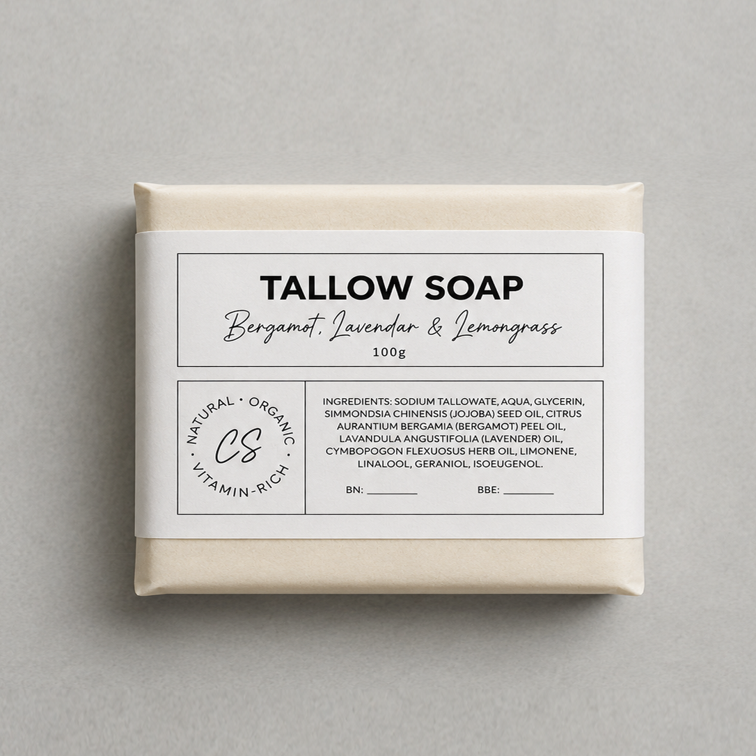 A rectangular bar of soap wrapped in cream-colored paper and featuring a white label with black text that reads 'TALLOW SOAP Bergamot, Lavender & Lemongrass 100g'. The soap is photographed from directly above on a neutral, textured light gray background.