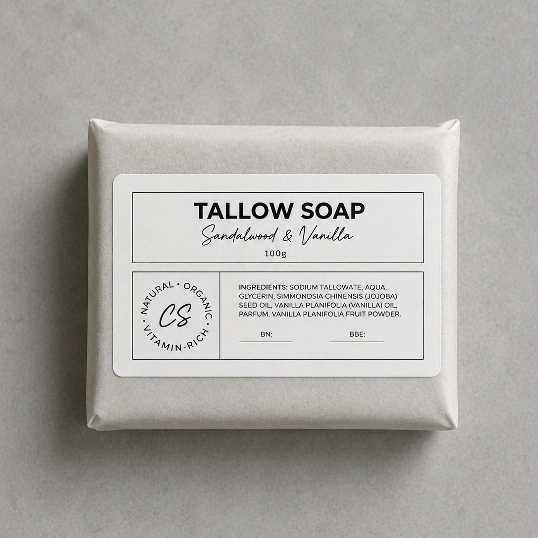 A square bar of Tallow Soap in Sandalwood & Vanilla scent, wrapped in a light gray paper sleeve with a white label, photographed from directly above on a neutral gray background.